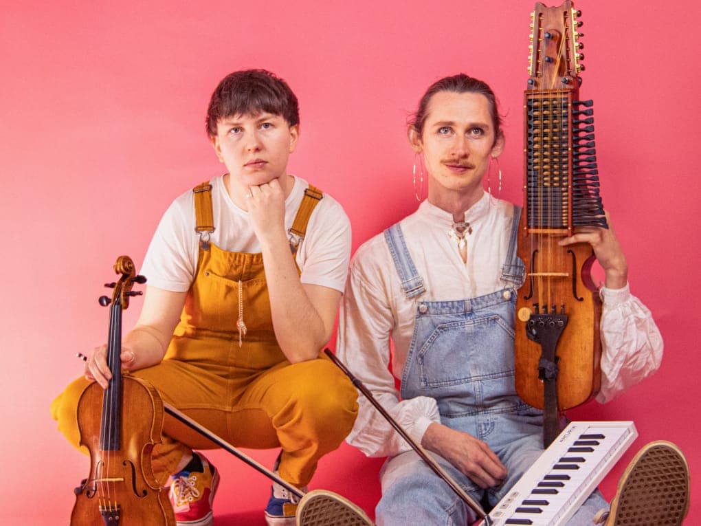 Julia Bengtson og Fredy Clue med violin, nyckelharpa og keyboard foran en lyserød baggrund