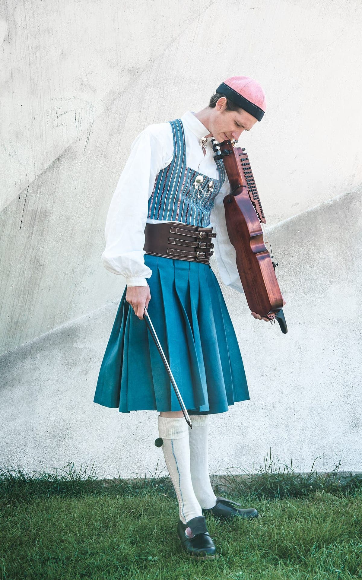 Fredy Clue står med nyckelharpa og bue iført den blå Bäckadräkten